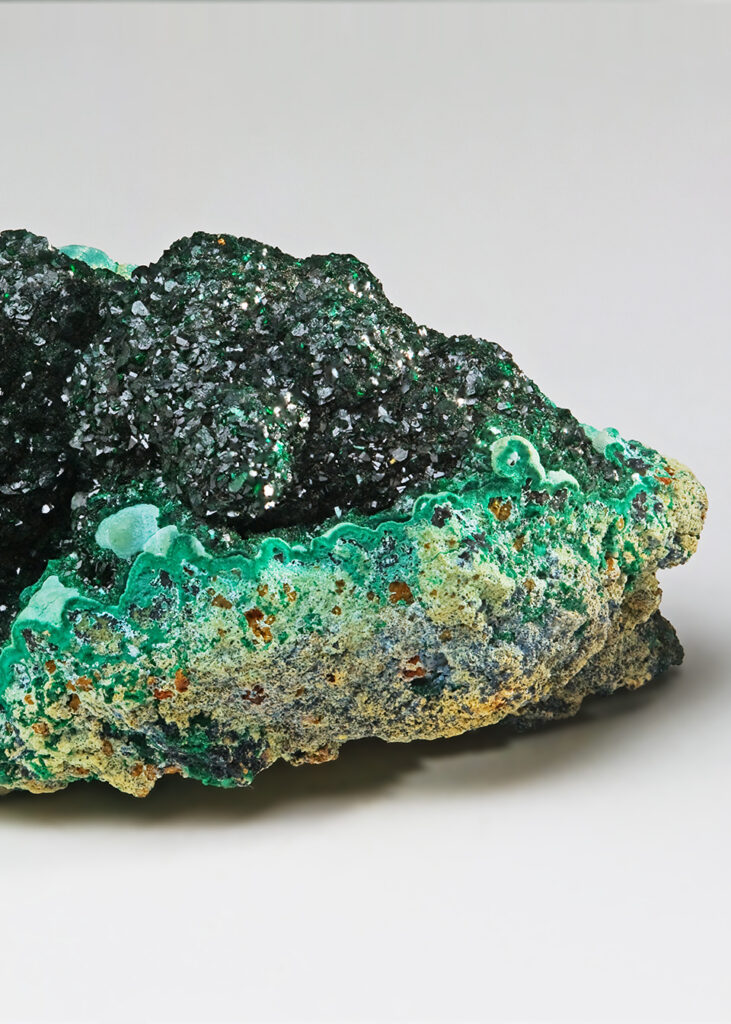 a rough malachite specimen showing dark green crystal formations atop lighter green and tan mineral layers